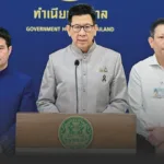Thai government official speaks at a podium during a briefing, with the government emblem visible on the lectern.