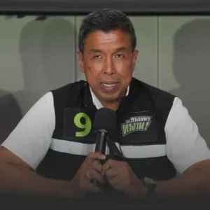 ชัชชาติยืนยันโปร่งใส ไม่กังวลหลังถูกร้อง ปปช ตรวจสอบปมโยกย้ายข้าราชการ » The Mainstream Male spokesperson speaking into a microphone at a press conference, wearing a black-and-white vest with a green number 9 badge