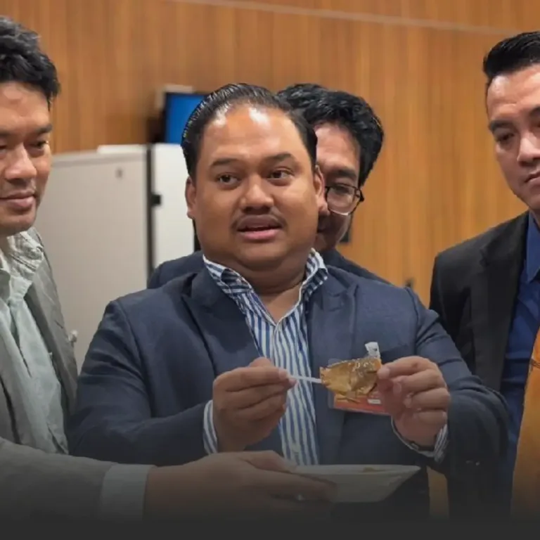 Man in a navy blazer holding a bite-sized pastry on a toothpick, presenting it to others in a formal setting.