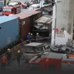 Truck and container crash scene with responders and damaged vehicles in a city street.