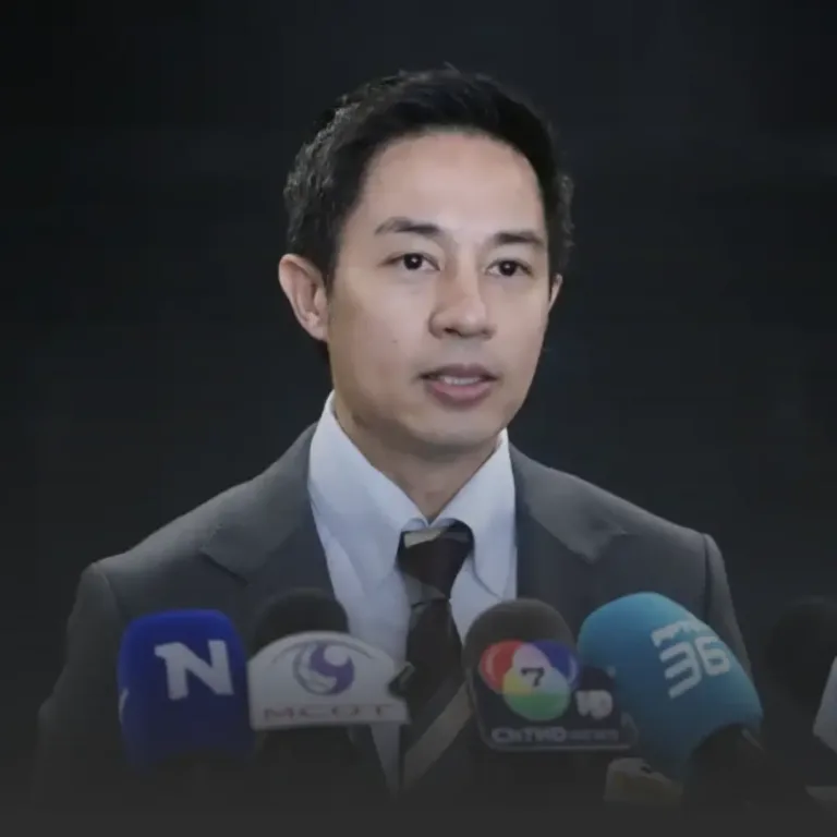 Man in a dark suit speaking at a press conference, microphones in front of him against a dark background
