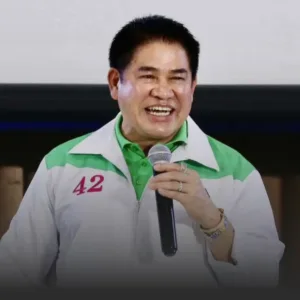 Smiling man in a white and green jacket with the number 42 on the chest, holding a microphone during a talk.