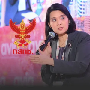 พิรงรองเตือนทีวีไทยเสี่ยงวิกฤตจากความล่าช้าแผนแม่บท กสทช » The Mainstream Female panelist speaking into a microphone at an event, with a red Garuda emblem and 'dnβ' logo in the background on a pink stage backdrop.