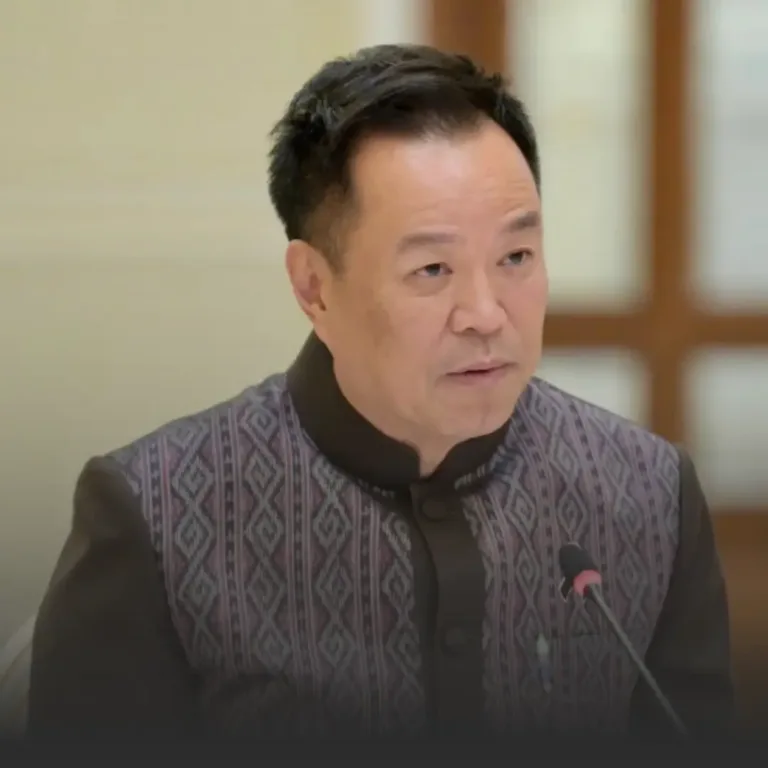 Man in a patterned jacket speaking into a microphone at a formal meeting room event