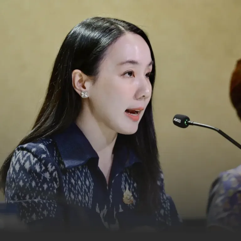 Woman with long dark hair speaking into a microphone at a panel, wearing a dark patterned blouse and decorative earrings.