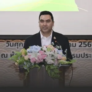 Man in a black suit delivering a speech at a podium with a large floral arrangement on the front.