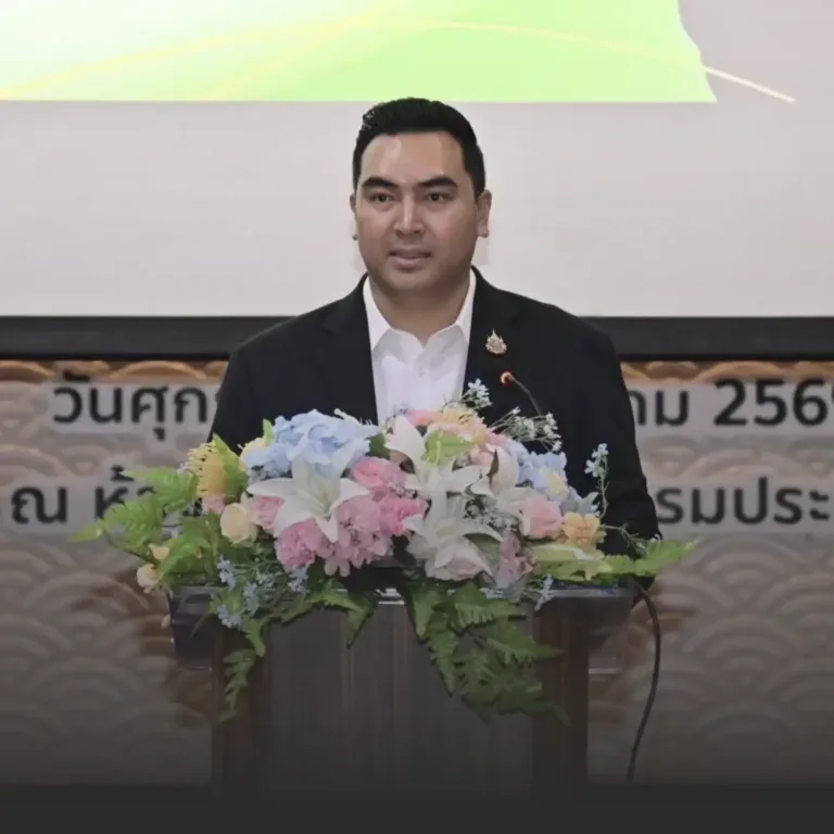 Man in a black suit delivering a speech at a podium with a large floral arrangement on the front.