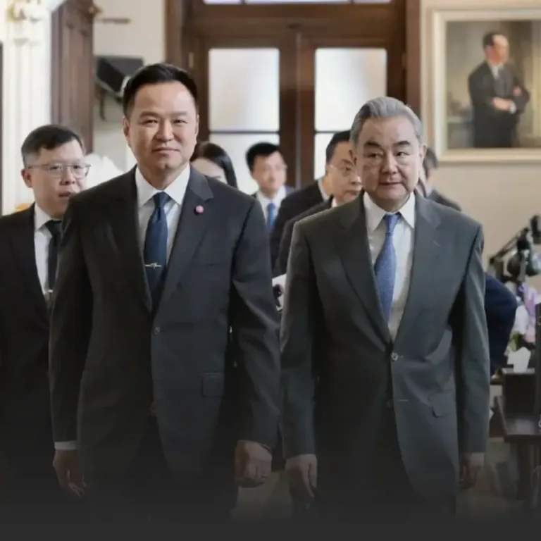 Two suited men walking side by side in a formal hallway, with others in suits following behind in a professional setting