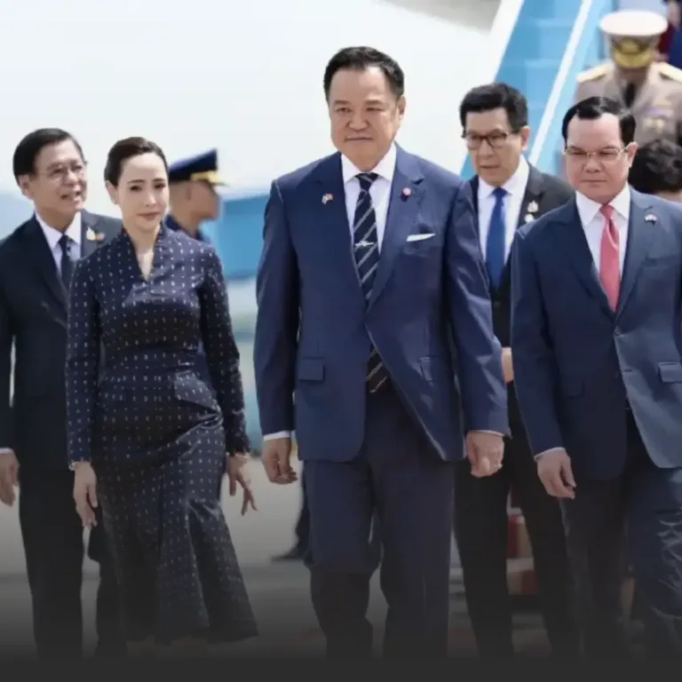 Group of formally dressed officials walking off an airplane, led by a man in a navy suit and striped tie, with a woman in a dark polka-dot dress beside him, others in suits follow.