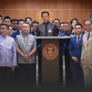อนุทินนำ สสภูมิใจไทย ยื่นร่างแก้รัฐธรรมนูญพรรคแรก » The Mainstream Group of formally dressed officials standing behind a podium with a gold emblem, in a wood-paneled room, during a formal event.