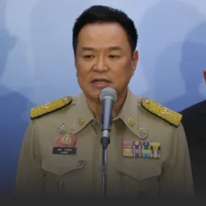 อนุทินย้ำ TH AI Passport โปร่งใส ชี้ ดีอีชี้แจงแล้ว » The Mainstream Male government official in a khaki uniform with medals speaking into a microphone at a podium.