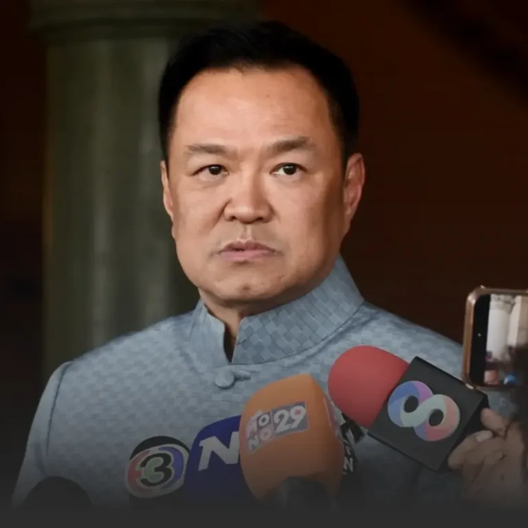 Man in a light blue mandarin-collar shirt speaks to reporters at a press conference, with microphones in front of him.
