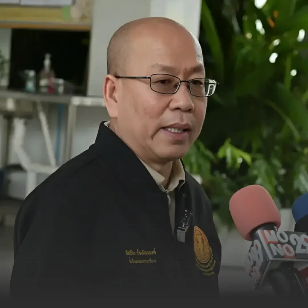 Man in glasses being interviewed, speaking to reporters with colorful microphones in a lobby or indoor garden setting.