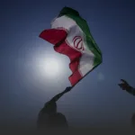 Iranian flag being waved by silhouetted figures with the sun bright behind it.