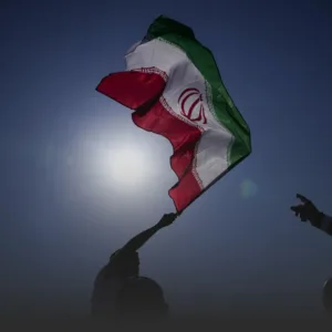 Iranian flag being waved by silhouetted figures with the sun bright behind it.