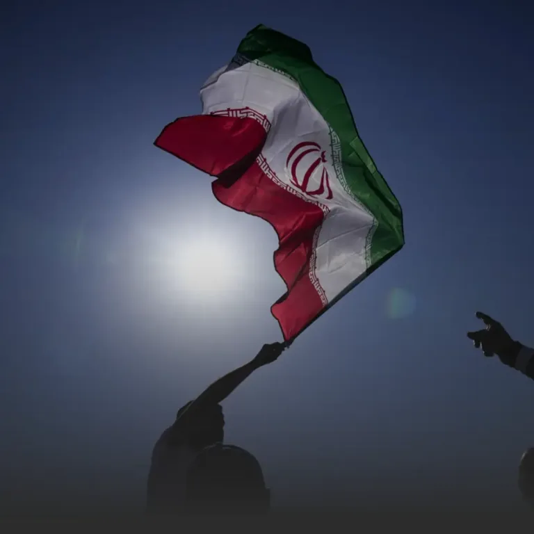 Iranian flag being waved by silhouetted figures with the sun bright behind it.
